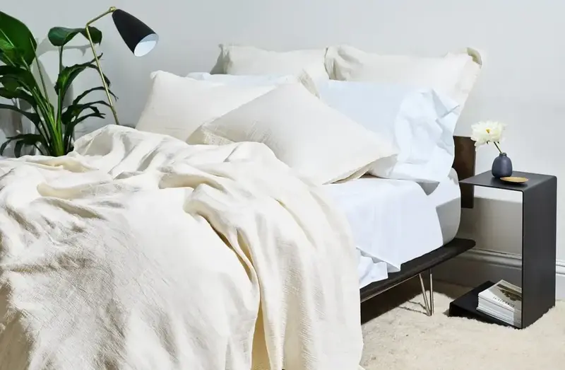 Black frame bed with white sheets and pillows and a beige throw blanket