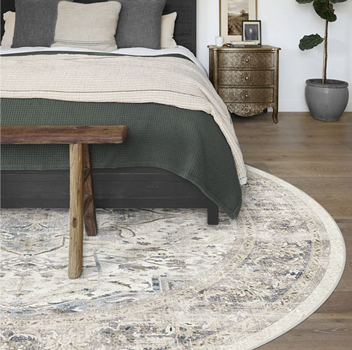 Large round rug under a grey upholstered bedframe in a cozy and bright bedroom