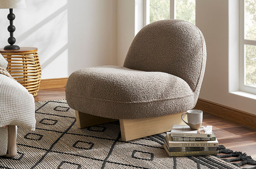 Light grey upholstered accent chair with a wooden base and black legs placed in an area rug