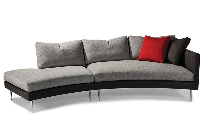 curved sofa with an architectural, swooping piece with low profile legs and two throw pillows,
