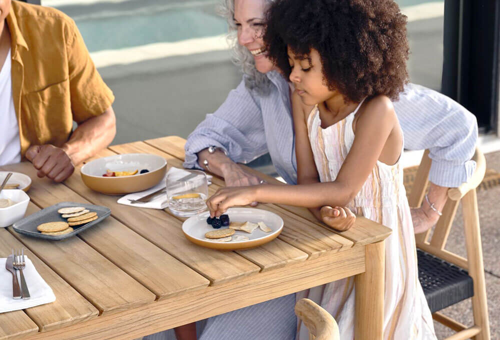 A family enjoying a meal together at a wooden outdoor table with a variety of food
