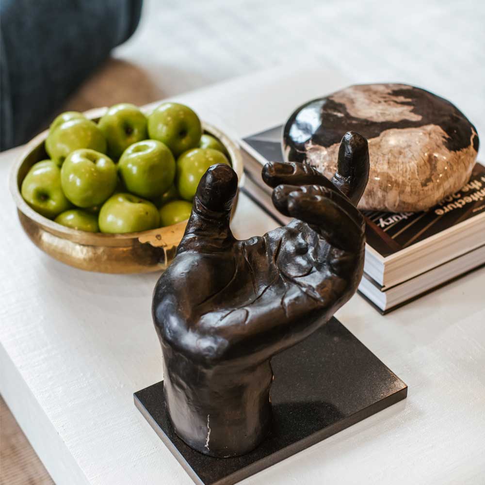 Decorative black hand in a white coffee table near a bowl with green apples