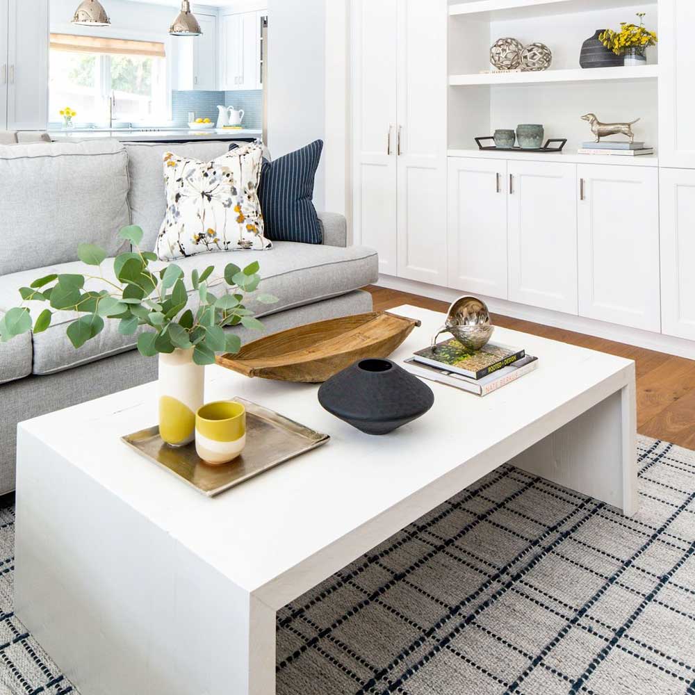 A white coffee table layered with a base, a plant and decor in a bright living room