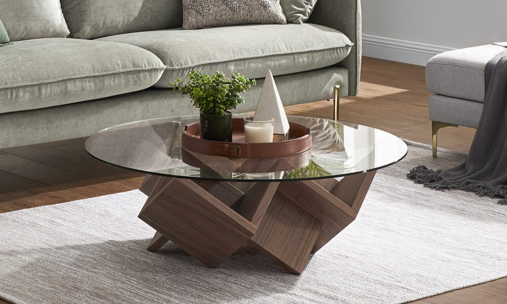 Coffee table with a round glass top and a geometric wood base on light gray rug in a living room