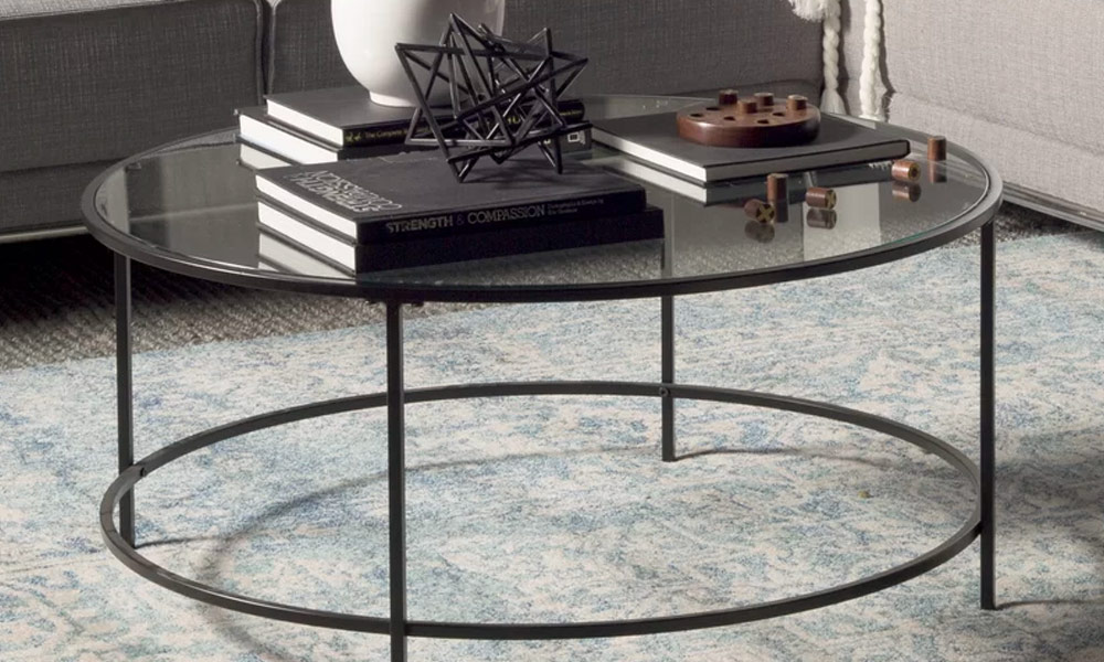 Round Coffee Table with glass top and black metal base with four straight legs with books in the top