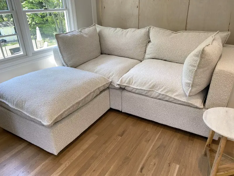 Colorful pillows and a peach blanket on a light gray couch in a bright living room.
