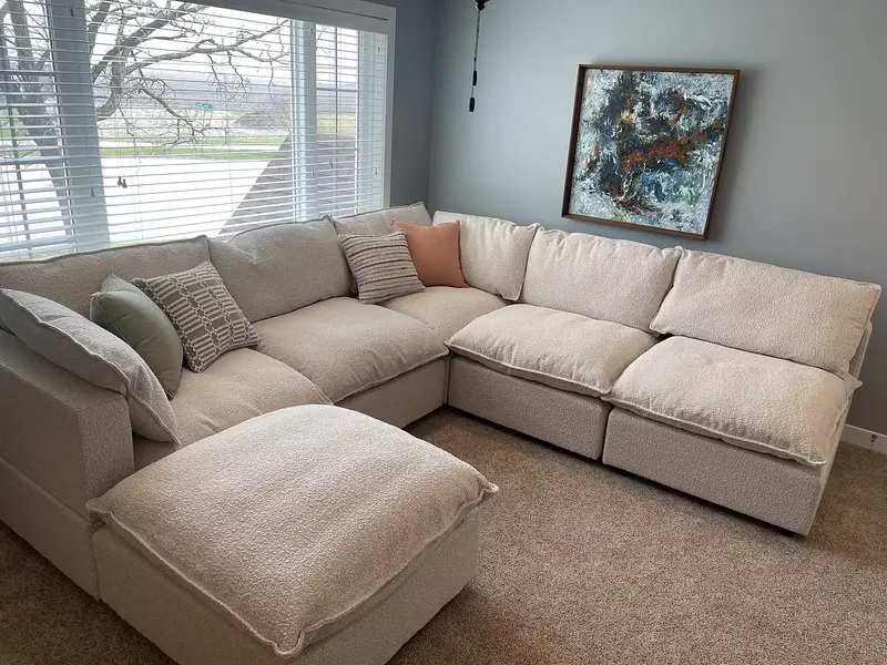 Colorful pillows and a peach blanket on a light gray couch in a bright living room.