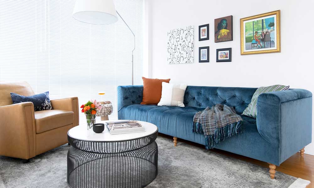 Living Room with a blue sofa, a light brown accent chair and a rounded black aluminum coffee table