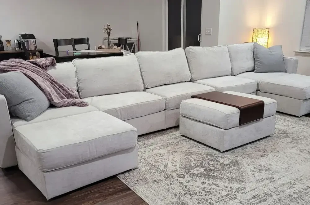 Light grey upholstered sofa with C-shape with throw pillows and blankets in a cozy living room