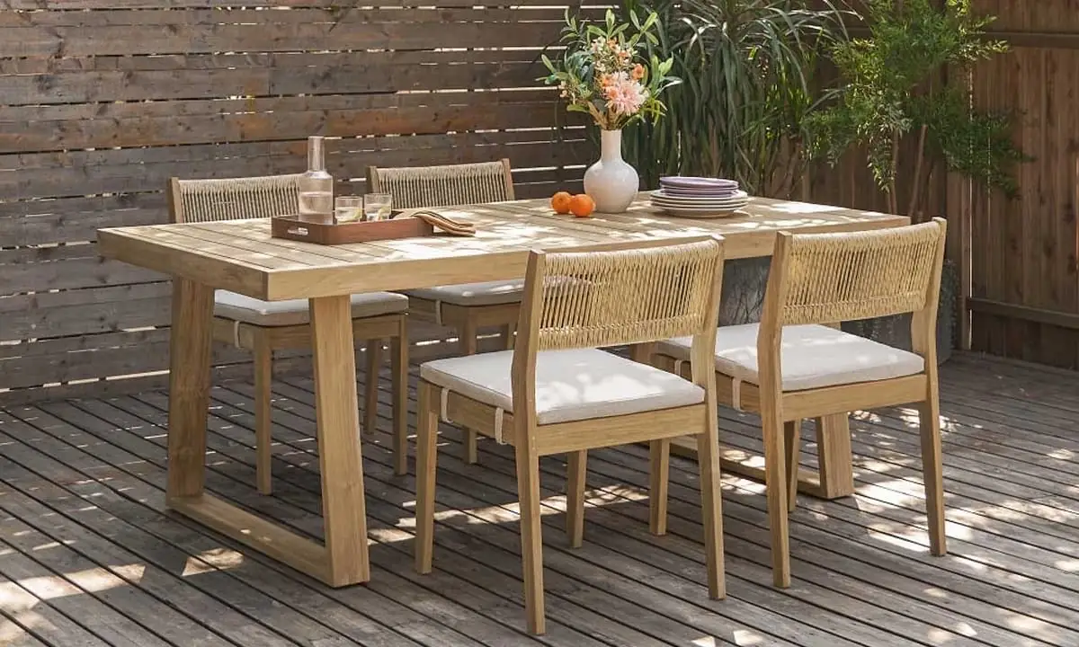 Wooden dining table with matching chairs on an outdoor patio set with plates and a vase of flowers