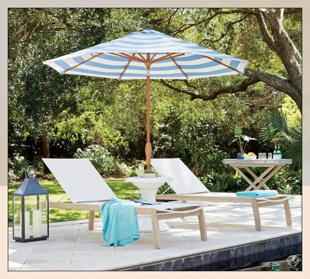 Light blue and white striped market umbrella with two pool lounge chairs near a pool
