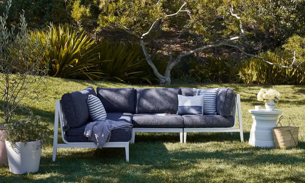 White Aluminum Outdoor L Sectional with blue cushions in a garden