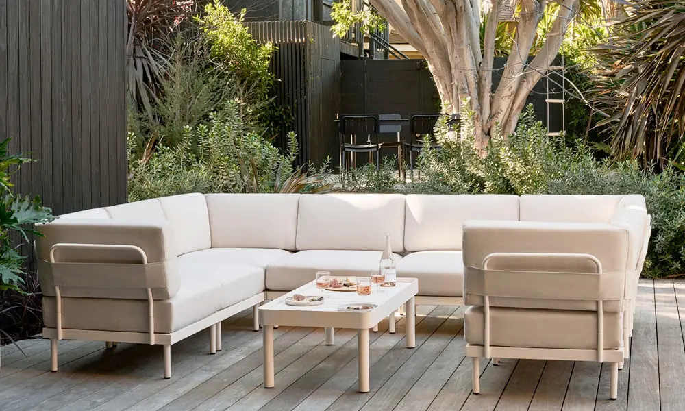 Beige outdoor Sectional with a beige coffee table in a patio near plants in a sunny day