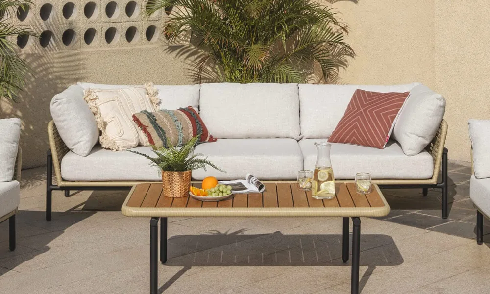  White sofa and two chairs on a patio, surrounded by lush green plants.