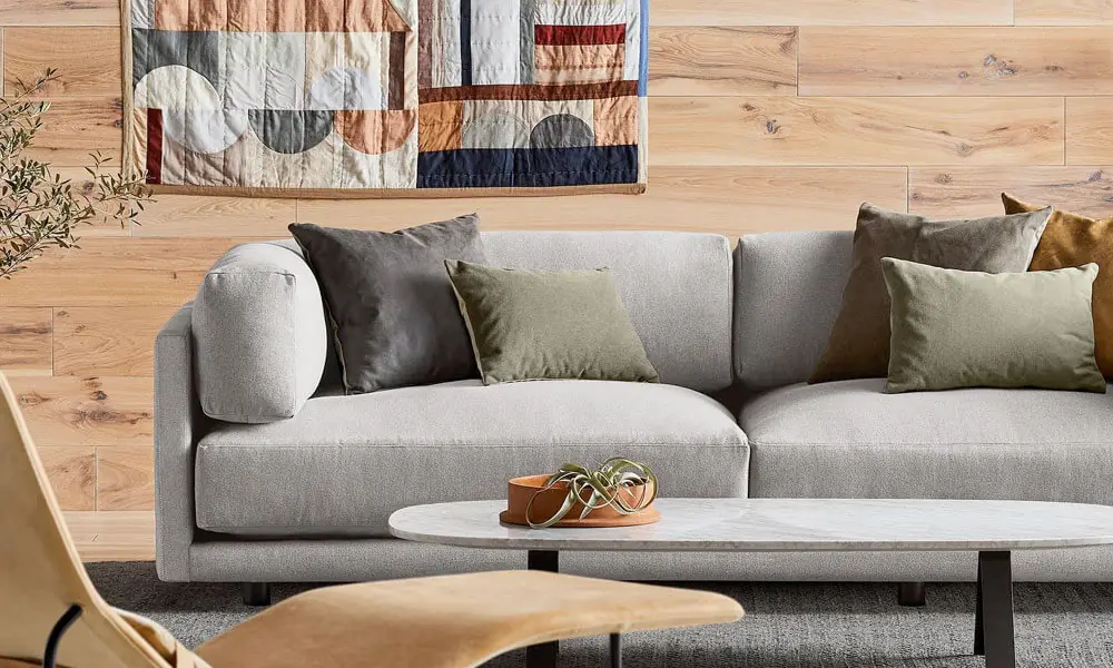 Grey upholstered sofa with dark grey throw pillows, an oval coffee table and a grey rug in a living 