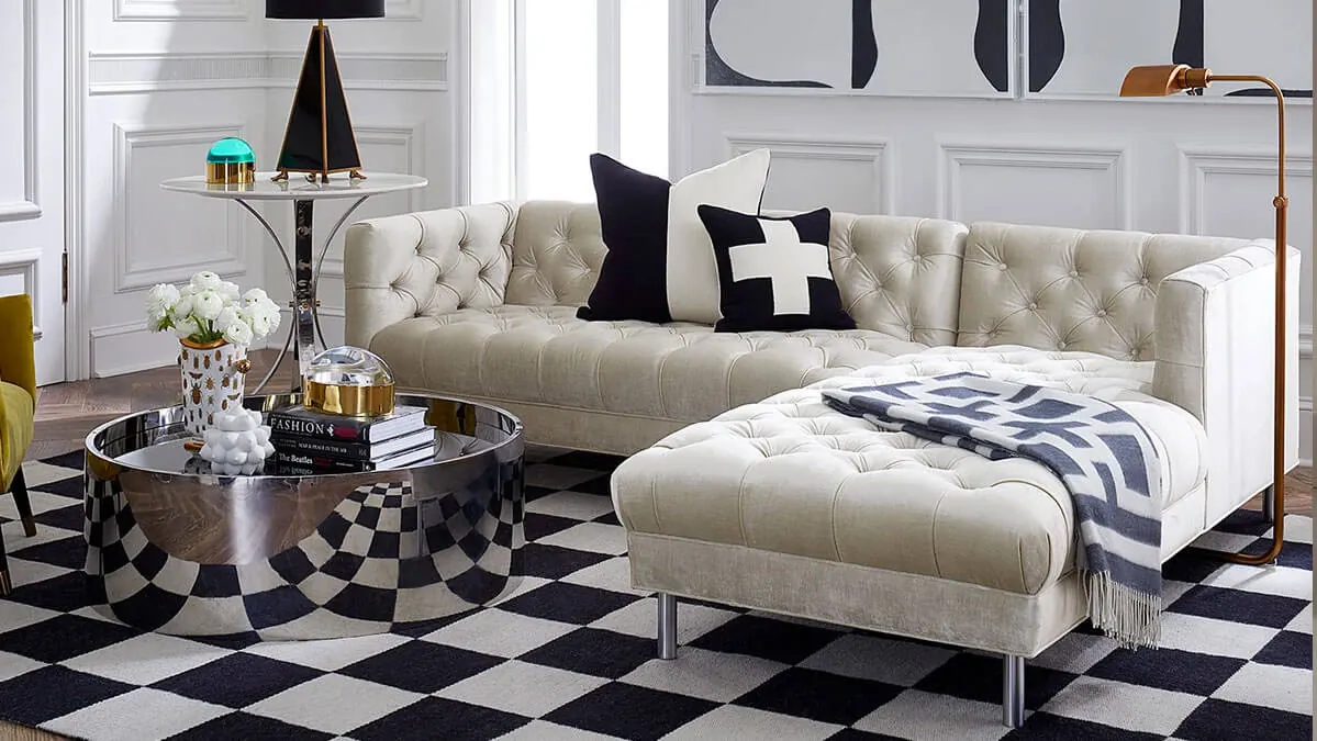 A white and black checkered rug with a beige sofa and a round silver coffee table in a living room