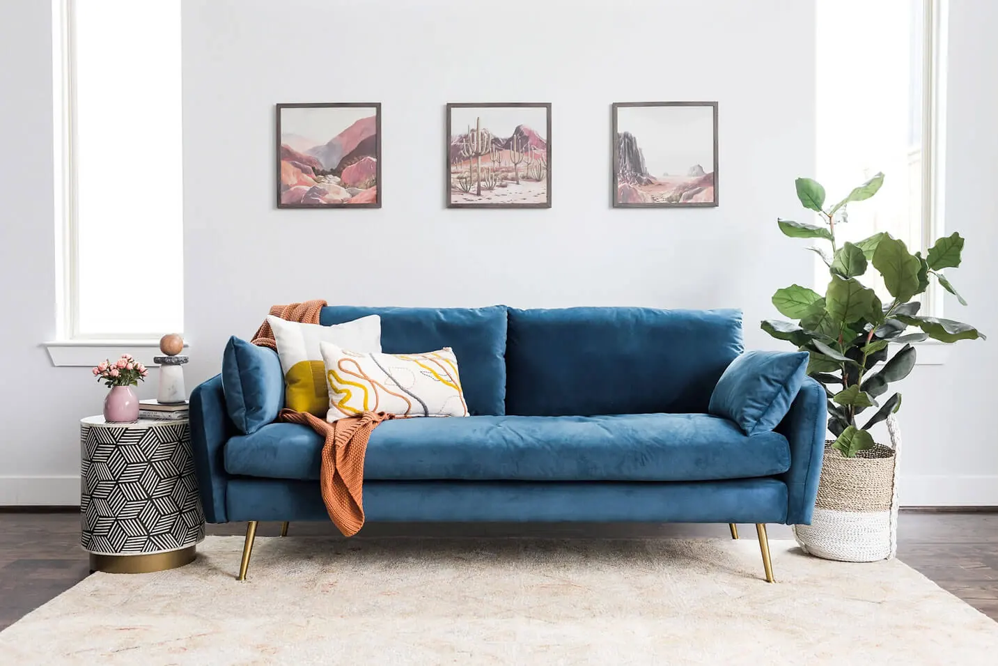 Blue sofa with golden legs, throw pillows, an orange throw blanket and a white rug