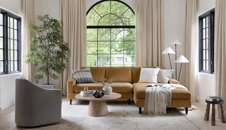 Brown sectional with a wooden round coffee table, a grey accent chair, and plants in a living room