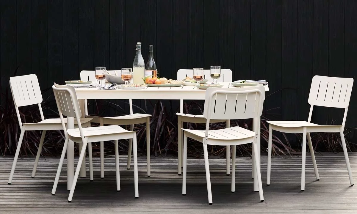 Outdoor dining setup with a white table set with plates, surrounded by six white chairs