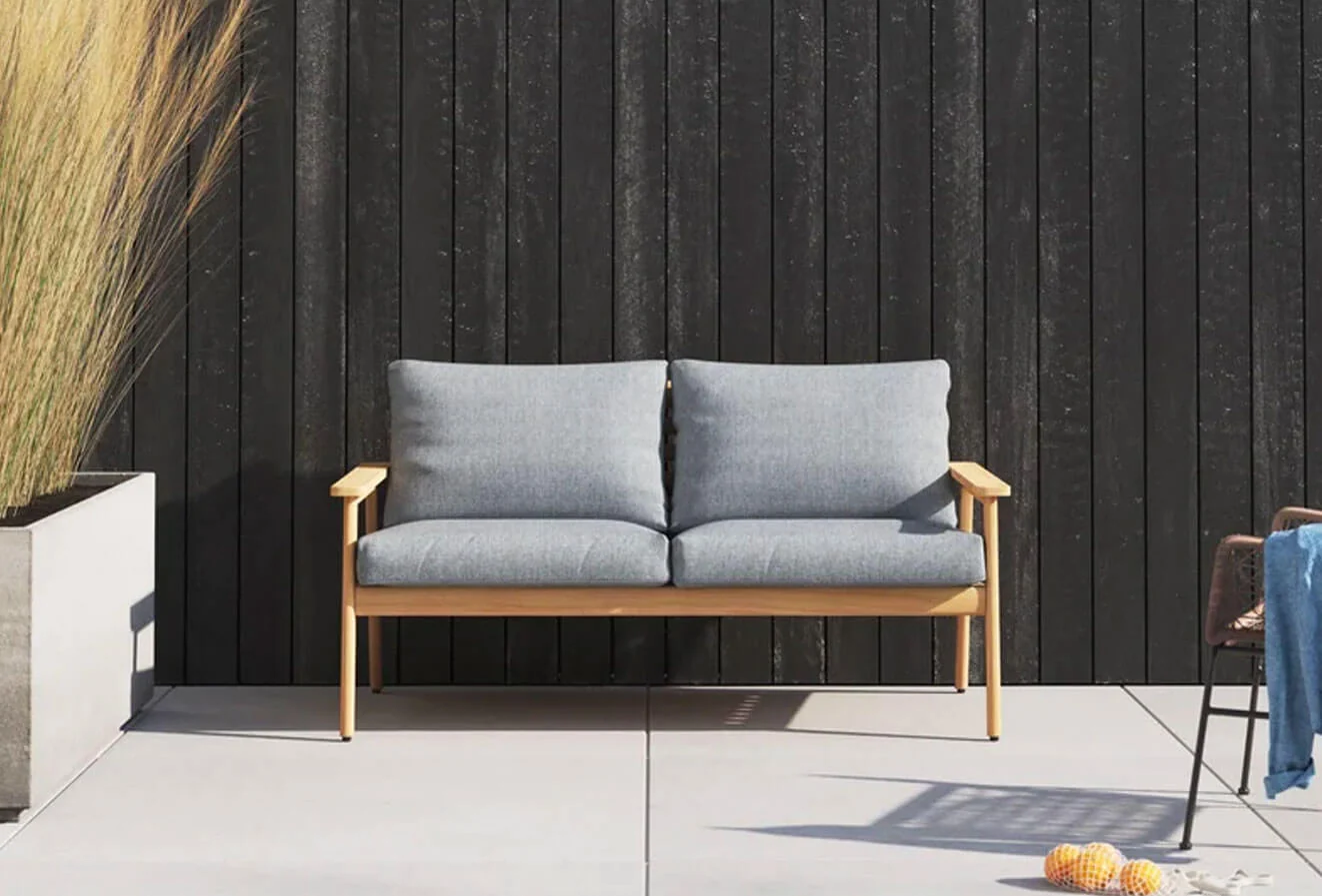 Teak outdoor loveseat with light grey cushions in a patio