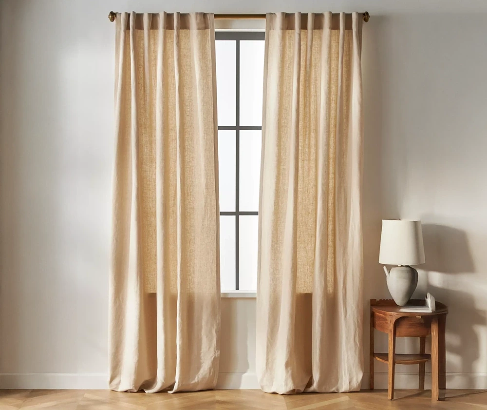 Light beige linen curtains draped over a large window, adding warmth and texture to a room
