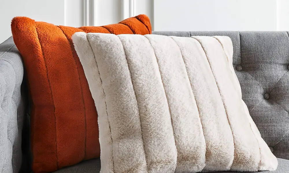 Faux fur Pillow in a grey couch, one is orange and the other one is white.
