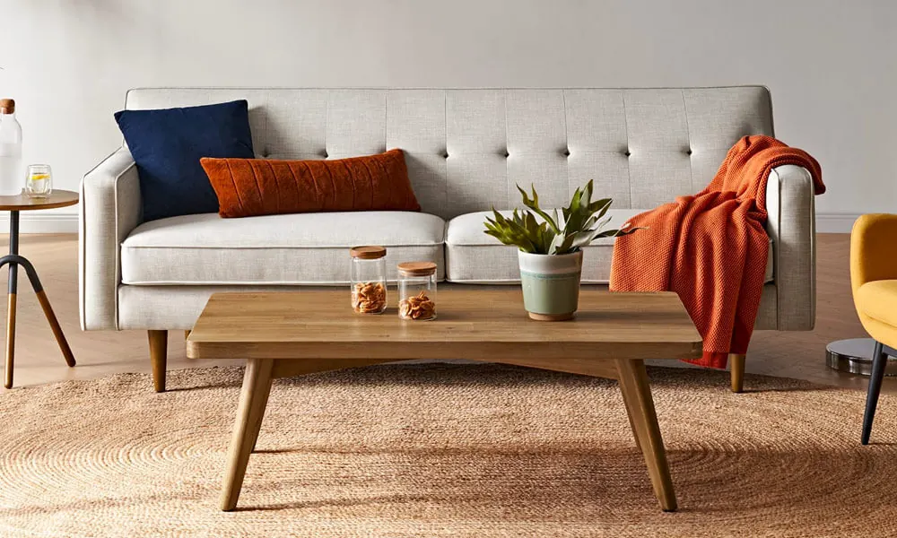 Wooden coffee table on a jute rug placed in front of a white sofa with red and blue pillows