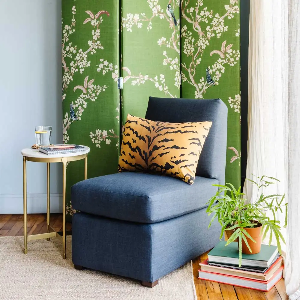 Blue upholstered Petite Slipper Chair in the corner of a room near the window and a green curtain