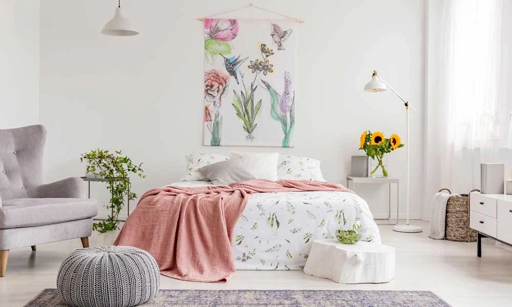 A cozy bedroom with a white bed, a gray chair, and a floral tapestry on the wall.