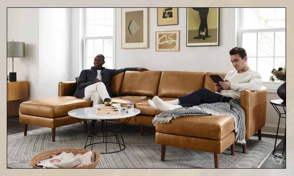 Two friends sitting in a brown Leather Sofa in a living room with a round coffee table and grey rug