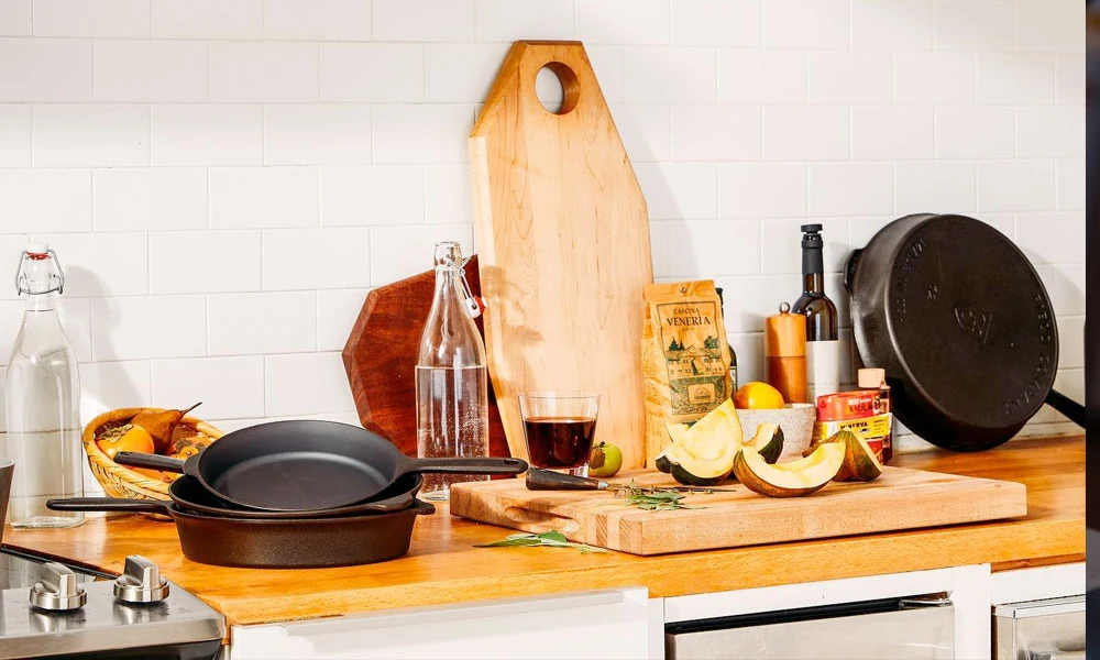 A kitchen counter featuring a wooden cutting board, a frying pan, and various fruits and bottles