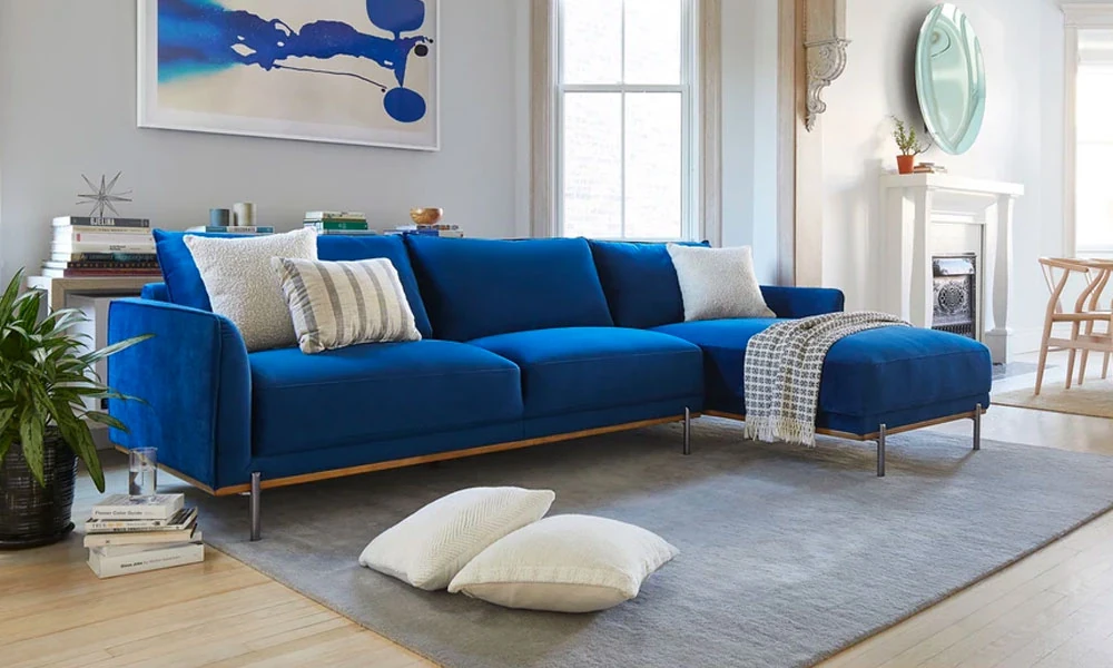 Blue velvet sofa un a bright living room with a grey rug underneath and a coffee table