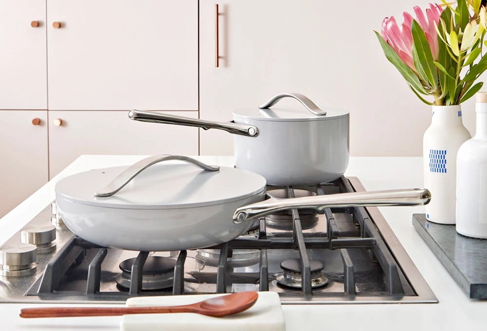 two gray saucepans with lids and stainless steel handles on a gas stove with a flower vase