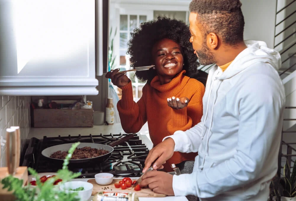 Smiling woman playfully holds a spatula while cooking with a man who is chopping vegetables