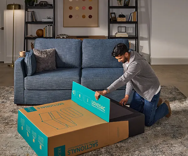 Person assembling a Lovesac Sactional from its shipping boxes in a living room
