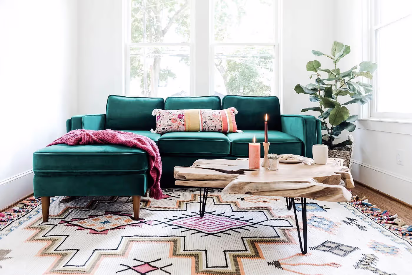 Green velvet sectional sofa in a bright living room with a patterned rug and wood coffee table