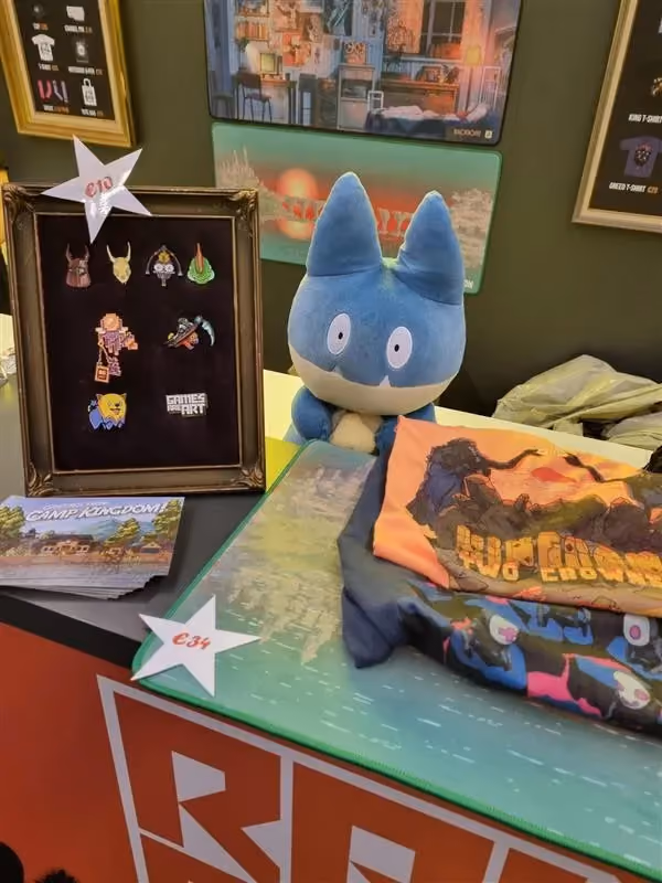 Several character pins, a plushie, t-shirts, and more merch on a Raw Fury event table.