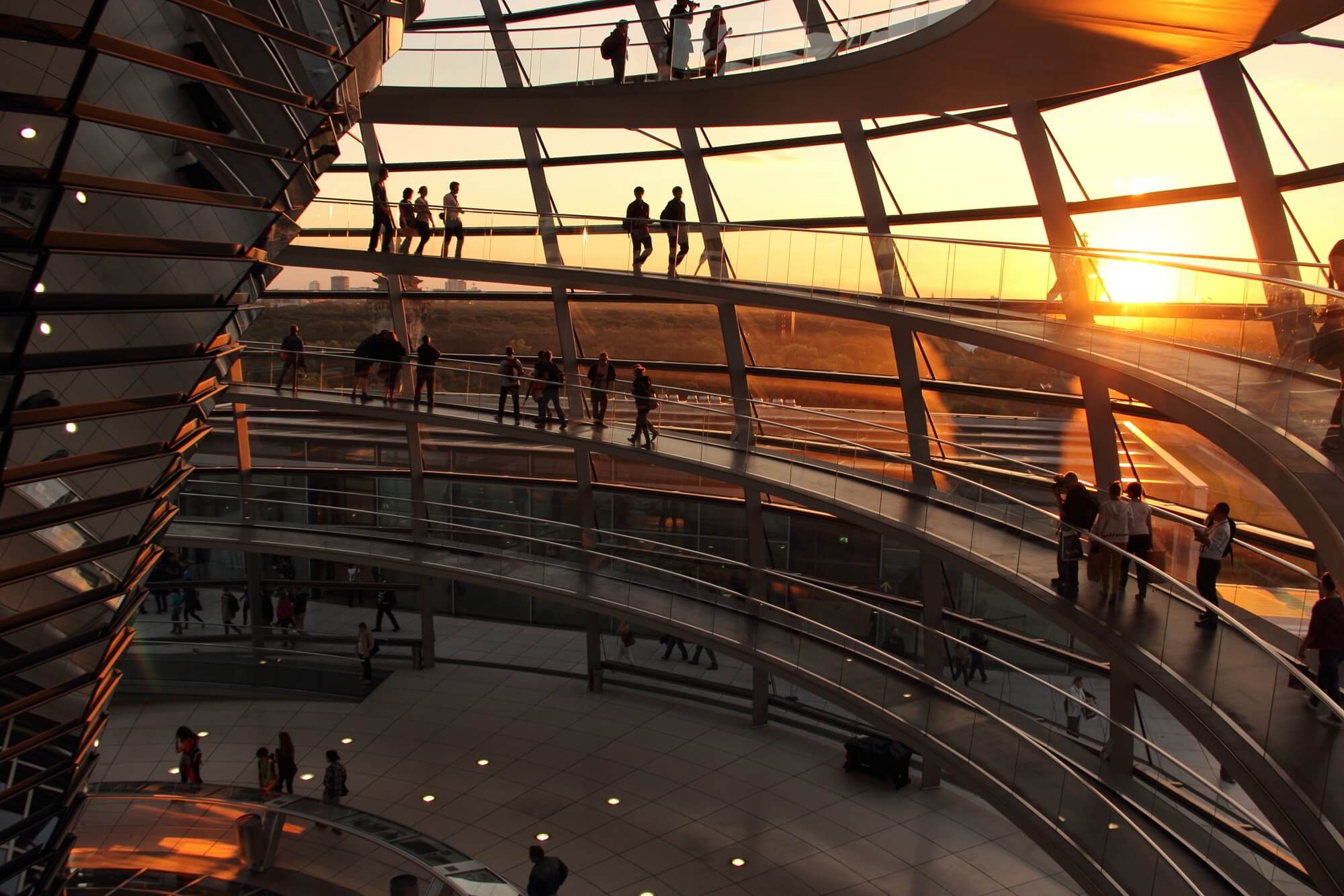 Visitors walking up the spiralling ramp inside the Reichstag glass dome at sunset.
