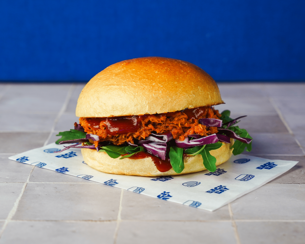 Sandwich au porc effiloché avec sauce barbecue, roquette et chou rouge dans un pain rond doré.