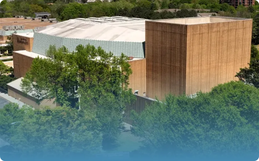 Aerial view of a modern building with wooden panel facades surrounded by green trees under daylight.
