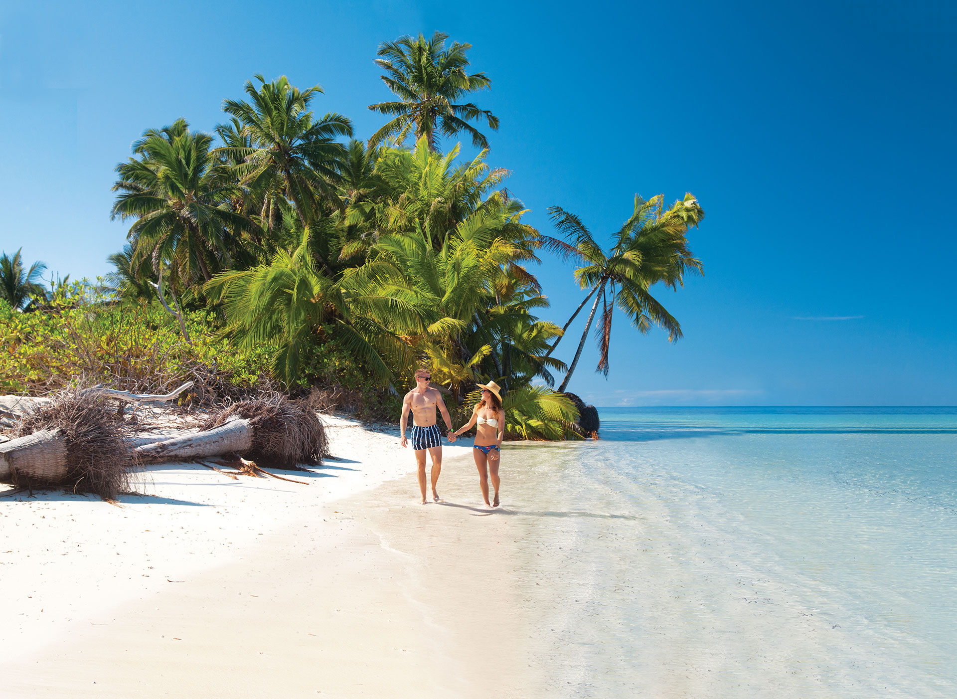 Couple walking on white sand beaches next to the ocean with palm trees in the background