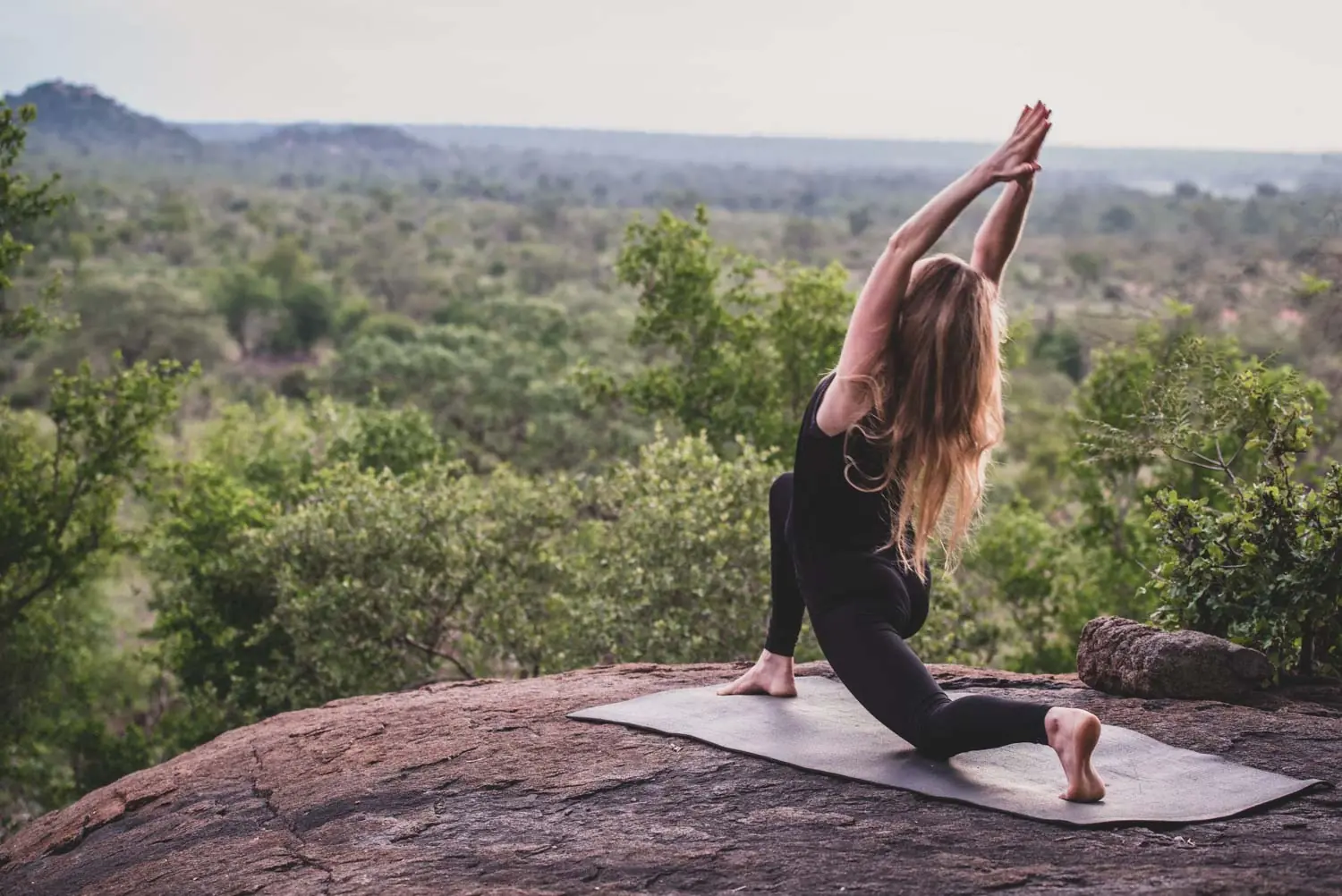 woman doing yoga on a boulder at the tree tops