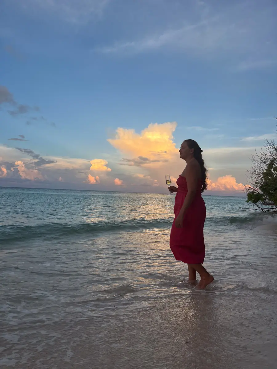 Woman standing in the sea holding a glass at sunset