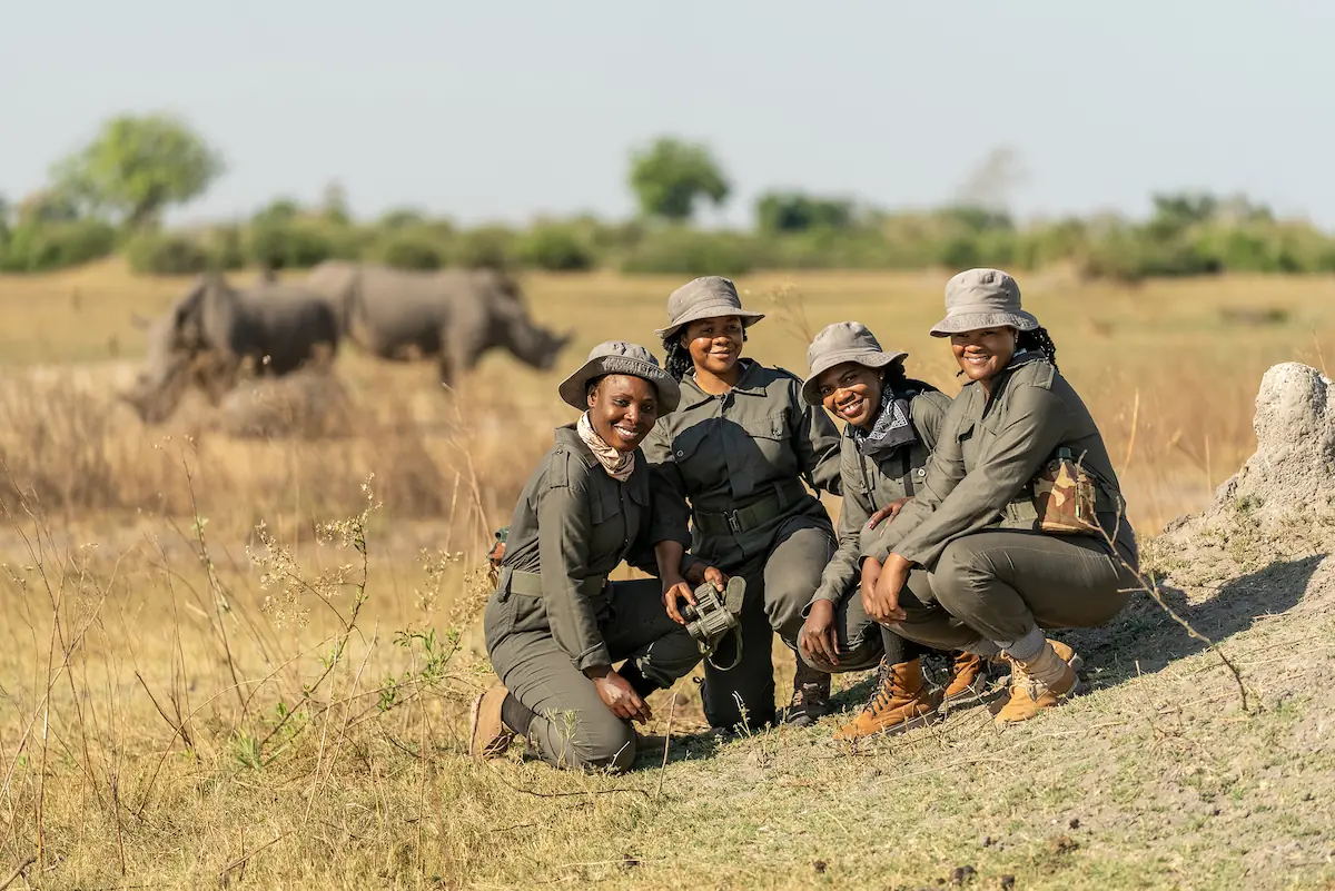 A group of female rangers crouches in front of two white rhinos