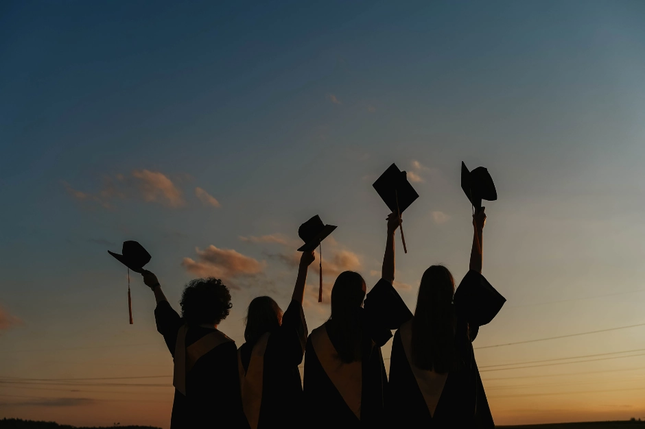 graduates holding up hats in sunset