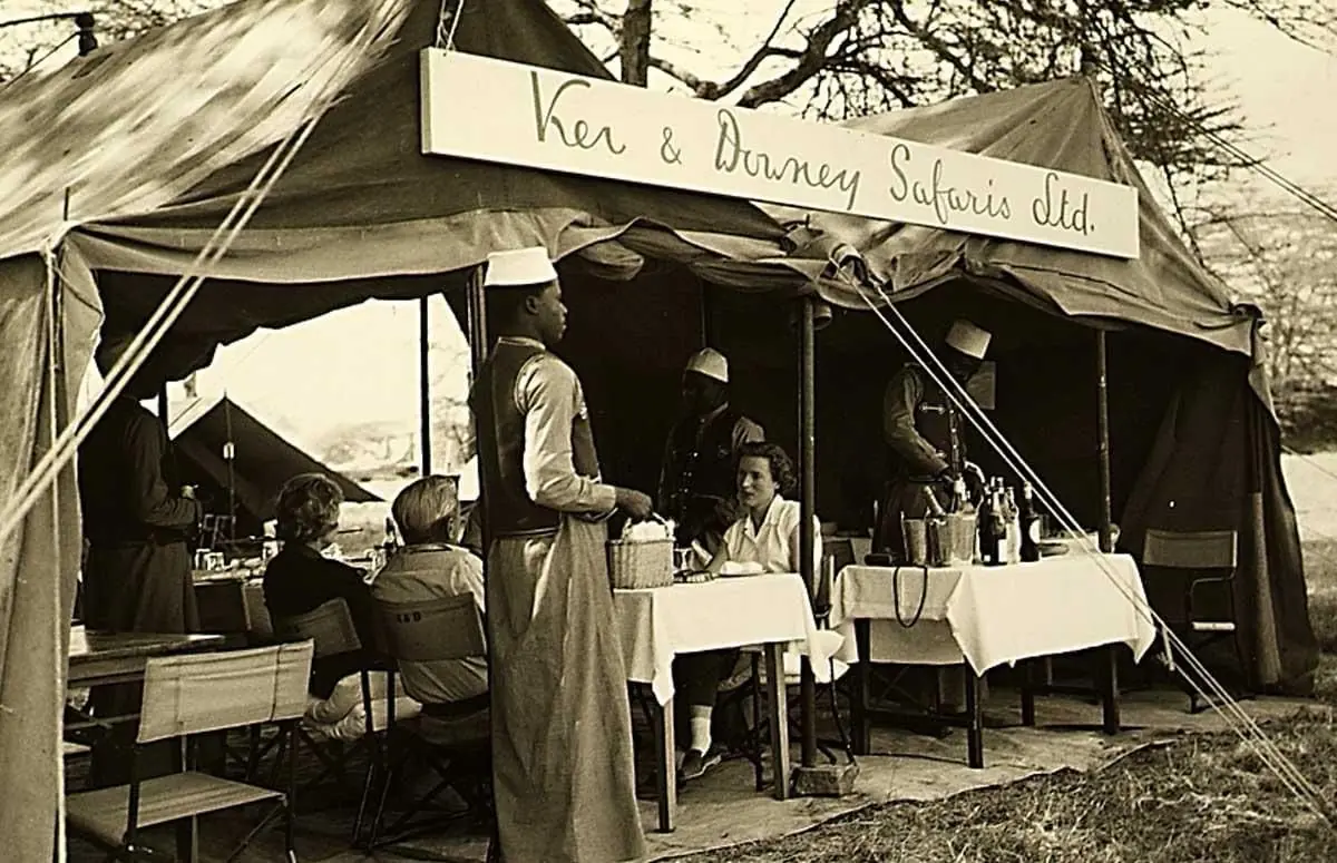 Black-and-white photograph of guests dining under a Ker & Downey Safaris canvas tent 