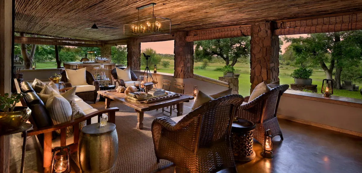 Covered veranda with stone pillars, wicker chairs and lanterns overlooking the lawn at Singita Castleton, South Africa