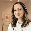 A smiling female dental professional in a white lab coat standing in an office