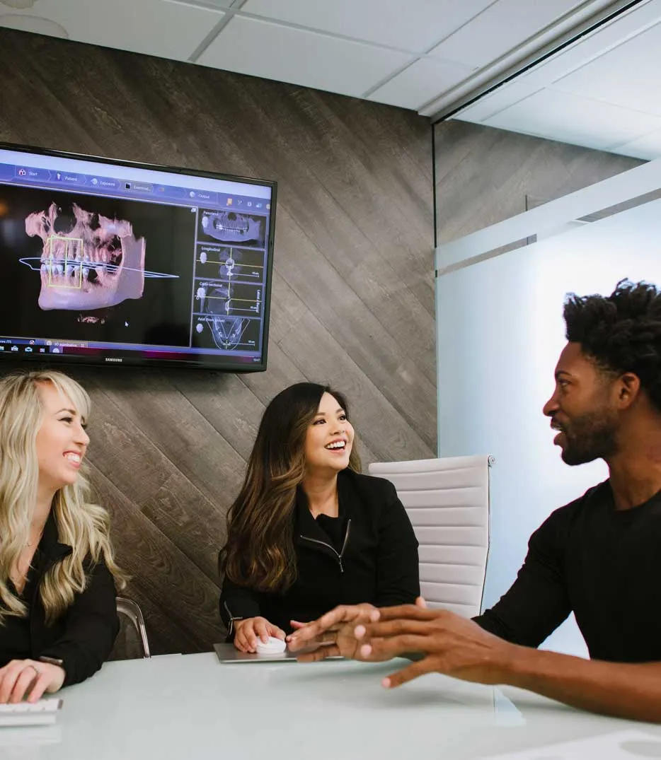 Photo of a dentist talking with a patient and team member.
