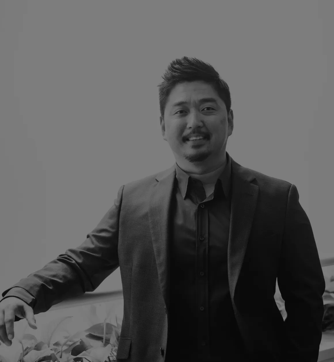 A black and white photo of Dr. Ben Liu, a smiling dentist in a suit leaning slightly forward, indoors, with a soft-focus background